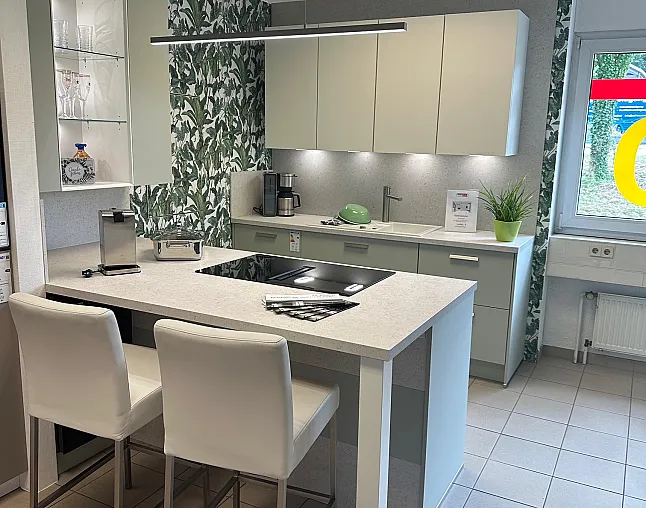 Moderne Küche mit grauen Schränken, Kochinsel mit Induktionskochfeld und zwei weißen Barhockern, dekorative Pflanzen- und Wandtapete.